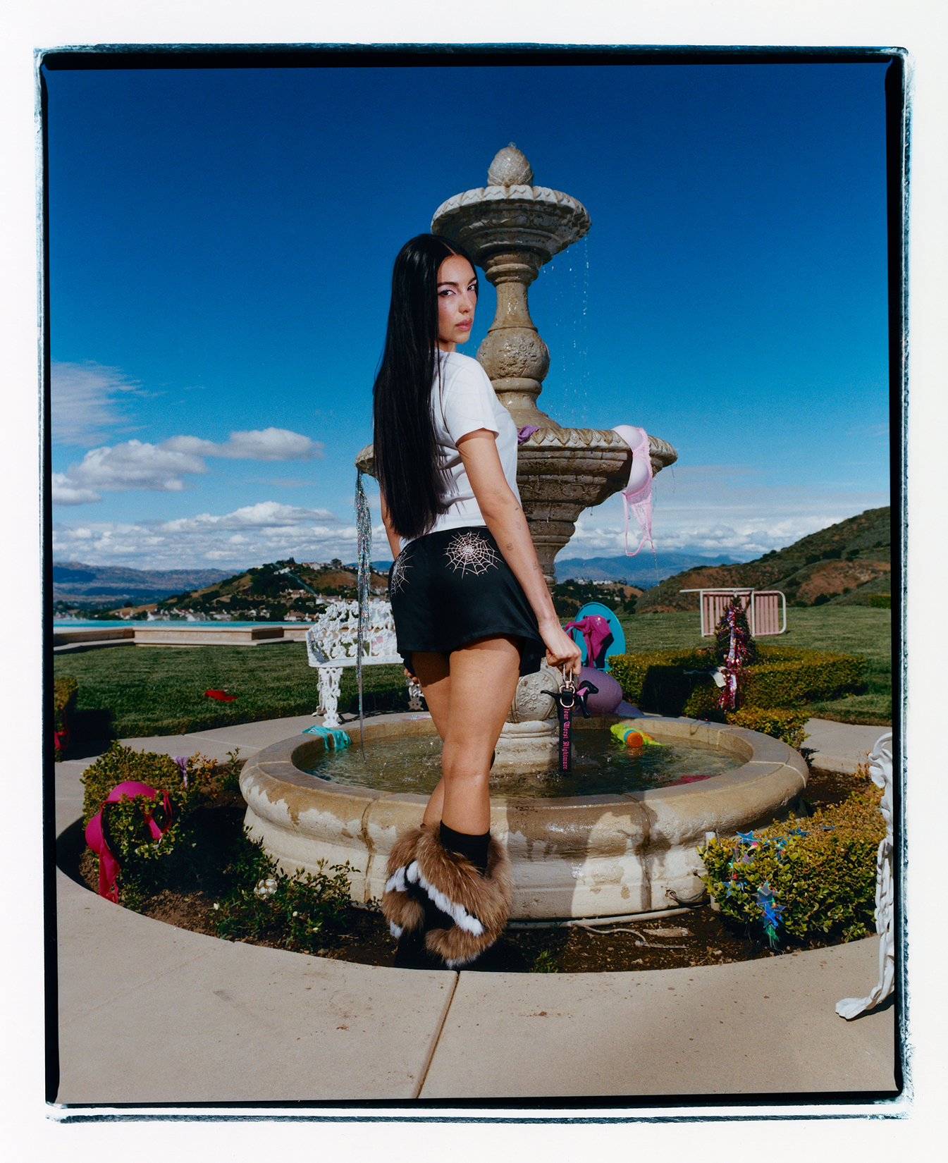 Model in a white t shirt and black shorts posing looking back at the camera in front of a water fountain on a sunny day